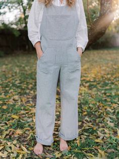 a woman wearing overalls standing in leaves with her hands on her hips and looking at the camera