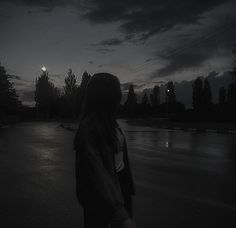 a woman standing in the middle of a street at night with her back turned to the camera