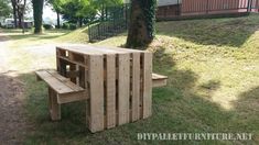 a wooden table and bench made out of pallets in the grass near a tree