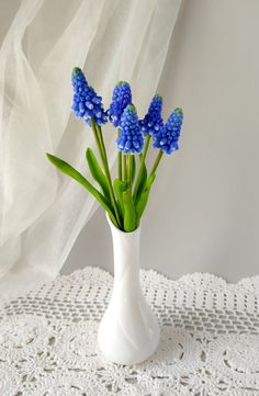 blue flowers are in a white vase on a doily