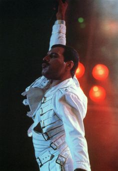 a man dressed in white performing on stage with his hands up to the sky and lights behind him