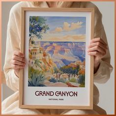 a woman holding up a framed poster with the grand canyon national park in front of her