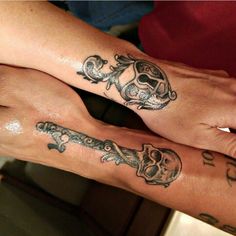 two people with matching tattoos on their arms holding each other's hands and looking at the camera