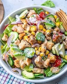 a salad with chicken, cucumber, tomatoes and onions in a white bowl