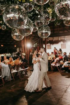 a bride and groom dancing in front of disco ball chandeliers at their wedding reception