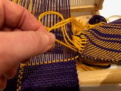 a person is working on weaving with yellow and blue yarn in a wooden box next to a pair of scissors