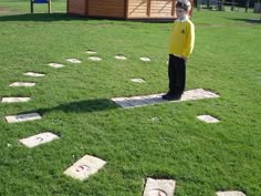 a young boy standing on top of a lush green field next to stepping stones in the grass