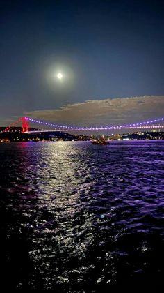 the moon shines brightly over the water as it passes under a bridge at night