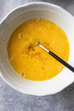 a white bowl filled with yellow liquid and a wooden spoon in the middle, on top of a gray surface