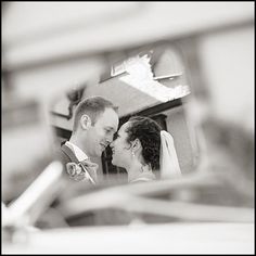 a bride and groom are reflected in the rear view mirror of a car as they look into each other's eyes