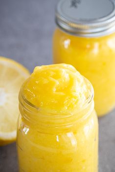 two jars filled with yellow liquid next to lemons