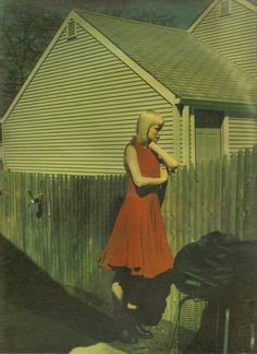 a woman in a red dress leaning against a fence