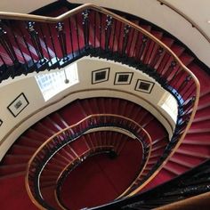 a spiral staircase in a building with red carpet and black railings on both sides