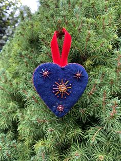 a blue heart ornament hanging from a pine tree with red ribbon on it