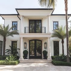 a large white house with lots of windows and palm trees in front of the entrance