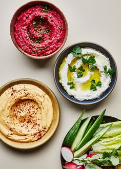 three bowls filled with hummus, celery, and radishes on top of a white table