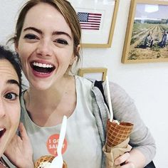 two women smiling and holding ice cream cones in front of their faces, with an american flag on the wall behind them