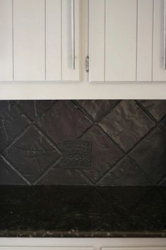 a kitchen with white cabinets and black granite counter tops on the backsplash is shown