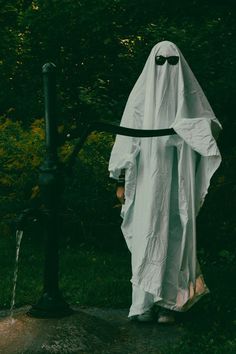 a person in a white ghost costume standing next to a fire hydrant