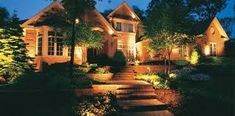 a house lit up at night with lights in the front yard and landscaping around it