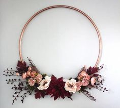 a circular metal frame with flowers and leaves hanging on it's side against a white wall