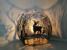 a glass bowl with a deer in the middle and trees around it on a table