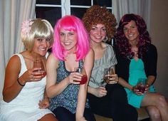 four women with pink hair are sitting on a window sill and holding wine glasses