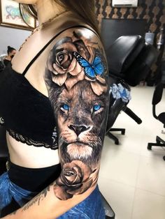 a woman's arm with a lion and butterfly tattoo on her left shoulder, which is covered in blue roses