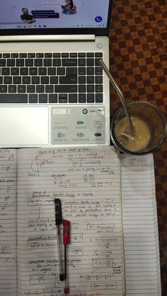 an open laptop computer sitting on top of a notebook next to a cup of coffee