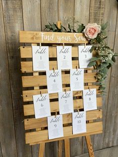 a wooden easer with seating cards on it and flowers in the center, sitting against a wood wall