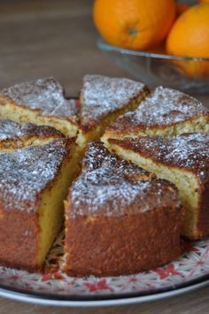 a cake on a plate with some oranges in the background and powdered sugar on top