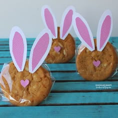 three cookies wrapped in plastic with bunny ears sticking out of them on a blue table