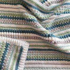 a crocheted blanket is laying on top of a tablecloth with blue, green and white stripes