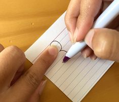 a person writing on a piece of paper with a pen in their left hand and another hand holding a marker