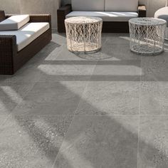 an outdoor living area with wicker furniture and large tiles on the floor, in shades of gray