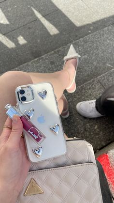 a person holding an iphone case with heart stickers on it, while sitting next to a handbag