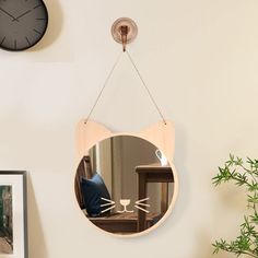 a mirror hanging on the wall with a cat's face in it and a plant next to it