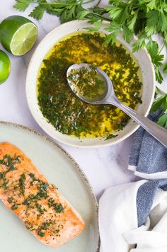 a white plate topped with salmon next to a bowl of green sauce and limes