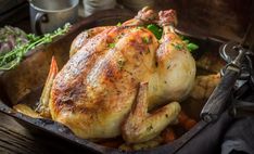 a roasted chicken in a roasting pan with carrots and parsley