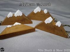 three pieces of wood with white mountains on them are shown in the shape of key chains