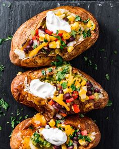 three loaded baked potatoes sitting on top of a black surface with sour cream and toppings