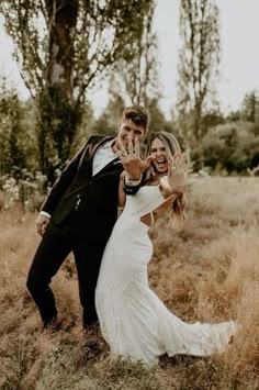 a bride and groom posing for a photo in the grass with their hands up to them