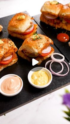 there are several sandwiches on the table with dipping sauces next to them and flowers in the background