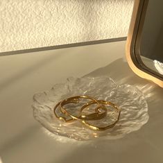 two gold wedding rings sitting on top of a clear glass plate next to a mirror