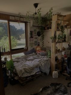 a bed sitting in a bedroom next to a window with lots of clutter on it