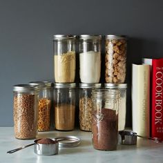 several jars filled with different types of food on top of a counter next to books