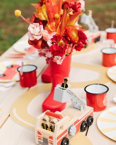 a table topped with red vases filled with flowers and firetruck figurines