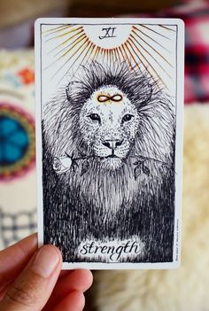 a hand holding up a tarot card with a lion on it