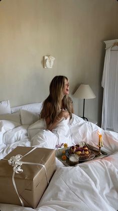 a woman laying in bed next to a gift box