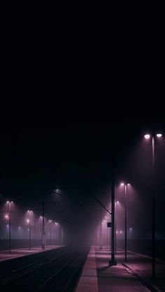 an empty train station at night with street lights on the platform and fog in the air